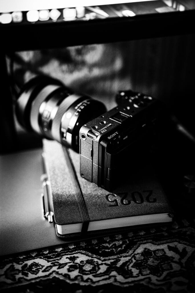 projektowanie stron www Czarno-białe zdjęcie aparatu fotograficznego spoczywającego na zamkniętym notesie z etykietą „2020”. Aparat odbija się w lustrze, a urządzenie znajduje się na wzorzystej powierzchni. Scena przekazuje atmosferę vintage, artystyczną. fotografia filmowanie augustów