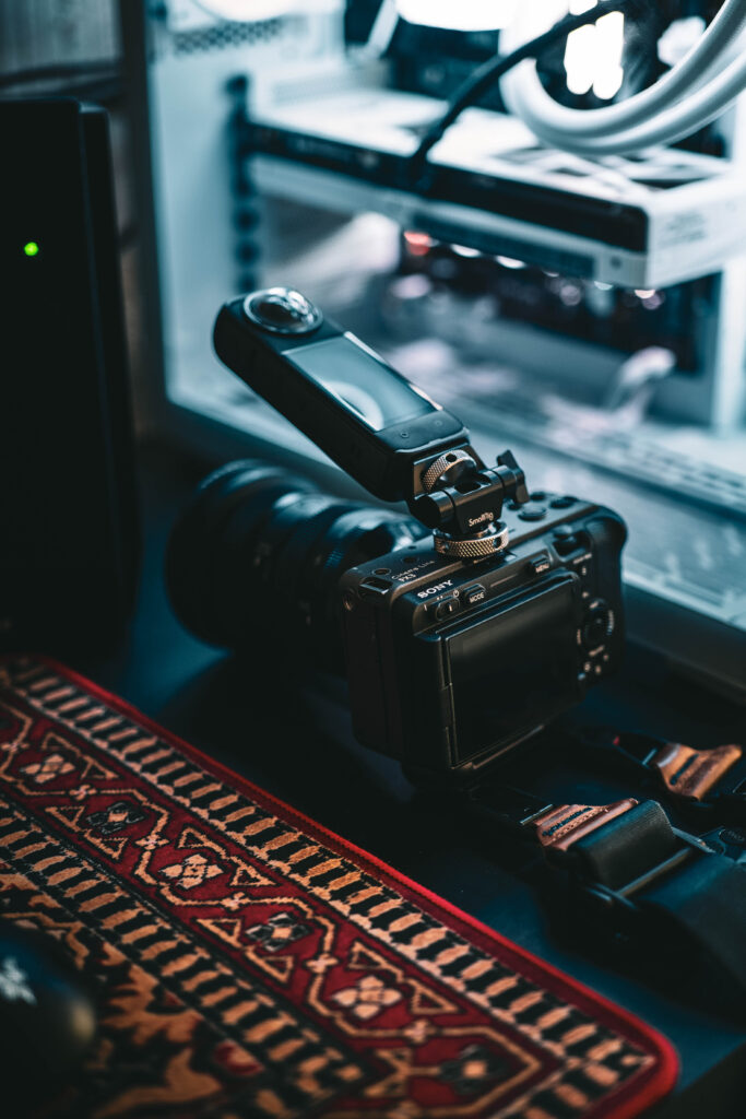 projektowanie stron www Cyfrowy aparat fotograficzny z dużym obiektywem i odchylanym ekranem leży na wzorzystym dywanie obok obudowy komputera i innego sprzętu elektronicznego. fotografia filmowanie augustów